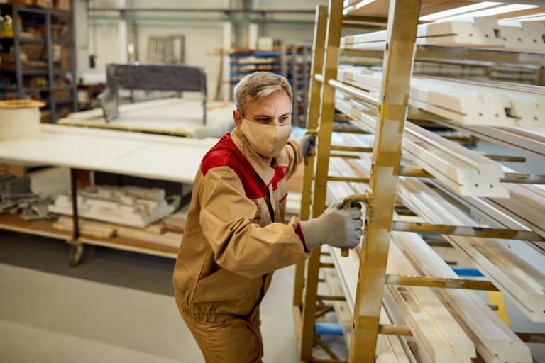 Male worker with face mask moving rack with processed wood at ca
